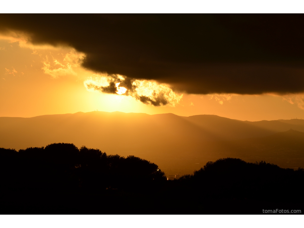 El sol, entre las nubes y la montaña